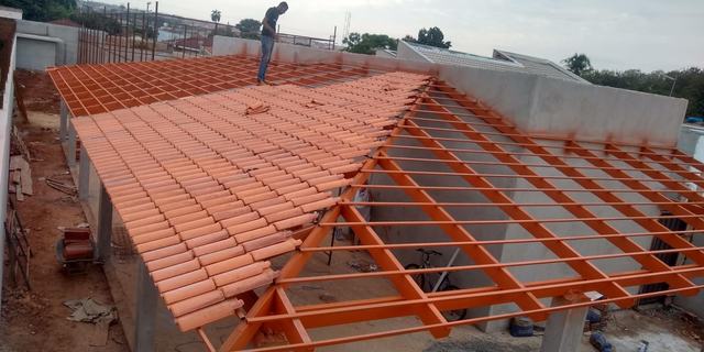 Estrutura metálica de telhado, em obra, recebendo telhas cerâmicas