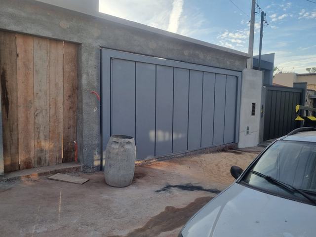 Portão deslizante cinza de chapa lisa em vão largo de garagem, com muro alto