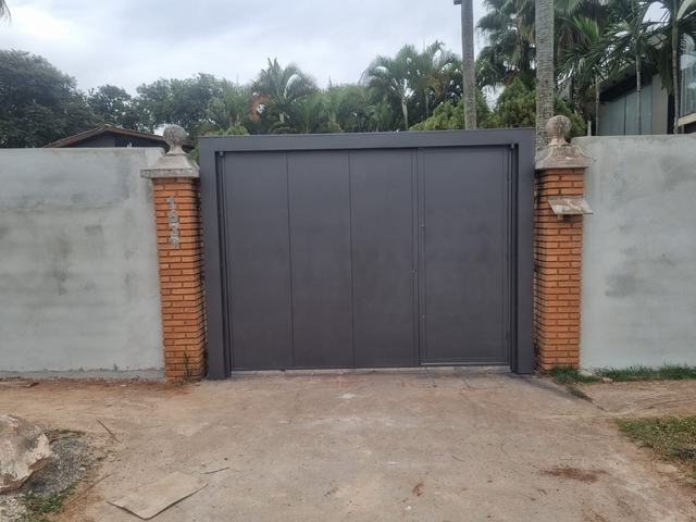Portão de abrir de duas folhas em chapa, pintado de grafite, entre pilares de tijolo